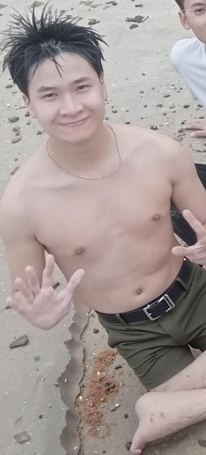 A young man sitting on the beach, smiling cheerfully while showing a peace sign