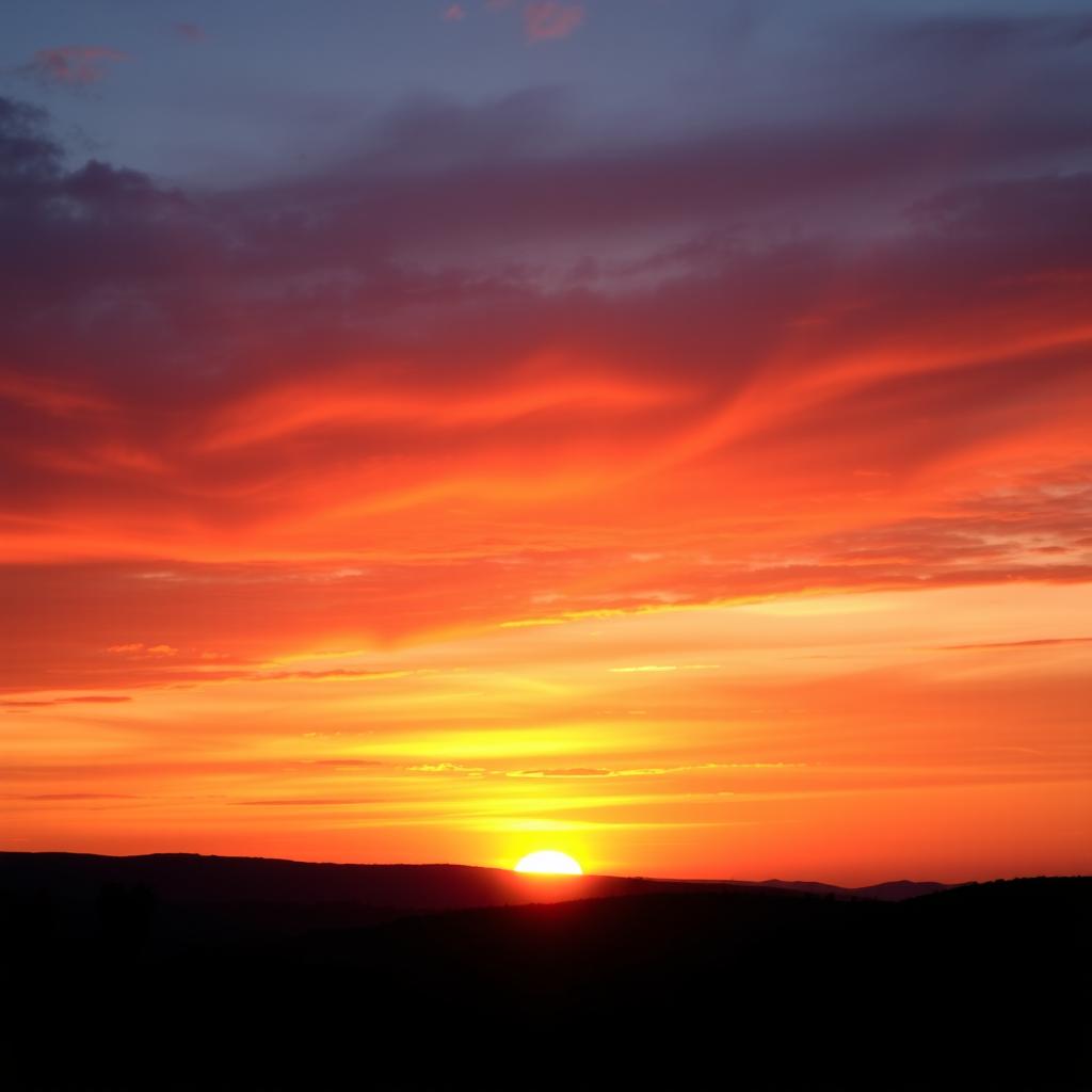 A breathtaking sunset scene with vibrant oranges, deep purples, and soft pinks blending in the sky as the sun dips below the horizon