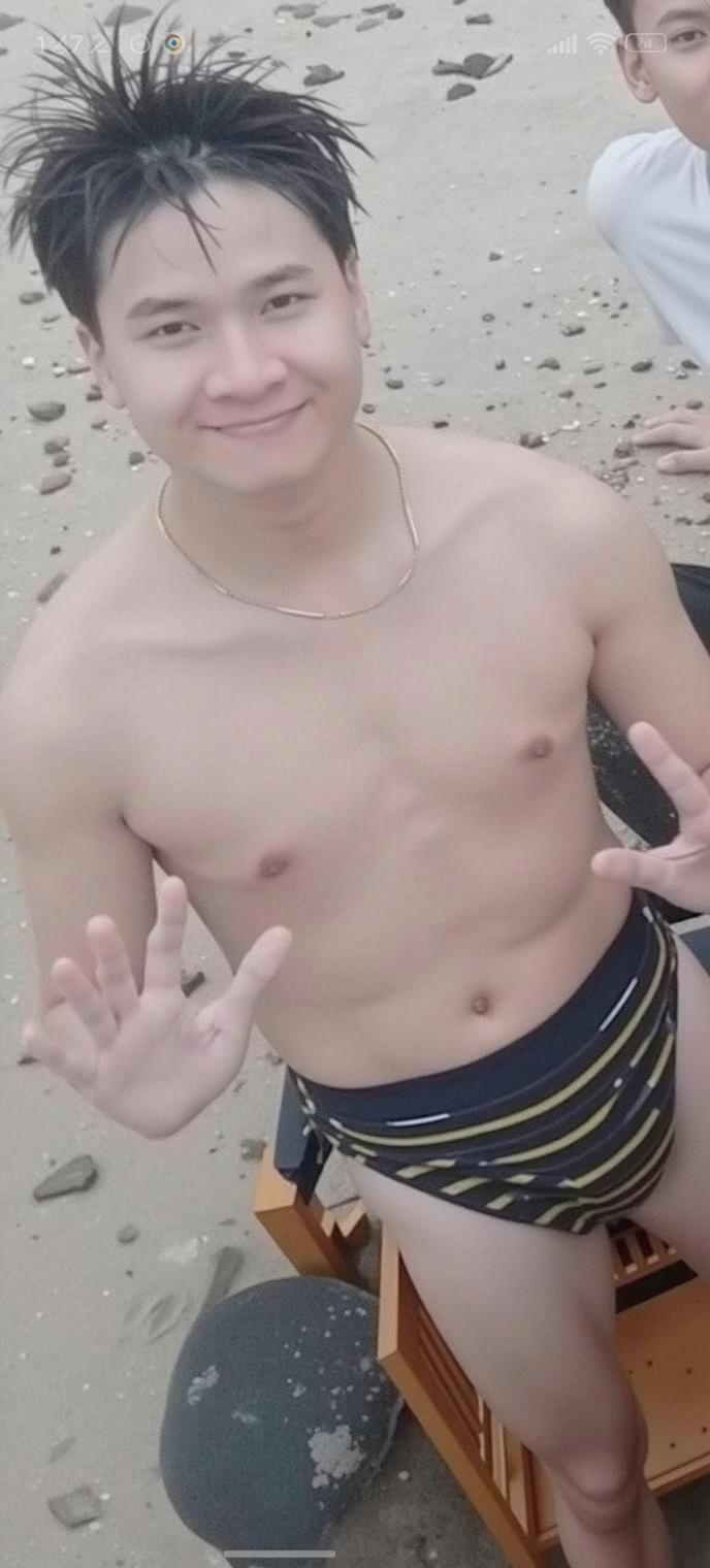 A young man sitting on the beach, smiling and posing with peace signs