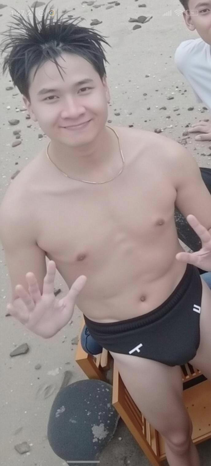 A young man sitting on a beach, wearing a snug-fitting swim brief