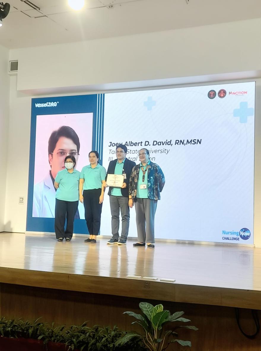 A professional event setting where a group of four individuals stands together on a stage, all smiling