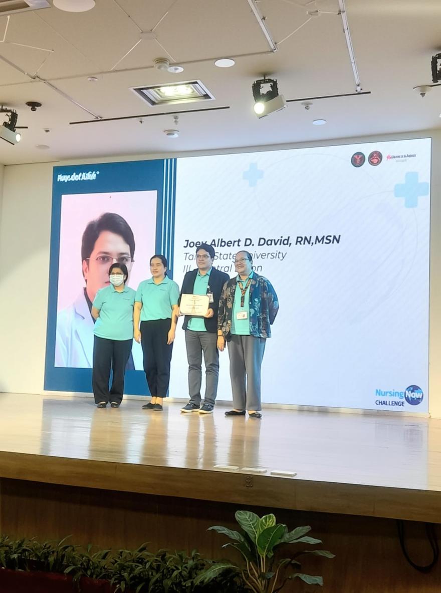 A professional healthcare conference scene featuring four individuals on a stage during a nursing awards ceremony