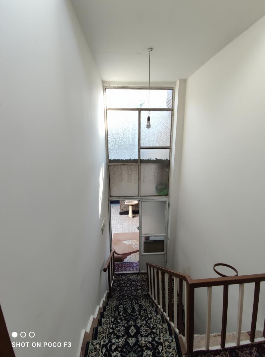 A staircase descending with black walls on both sides, leading to a landing with a view of a cozy outdoor area through a clear window