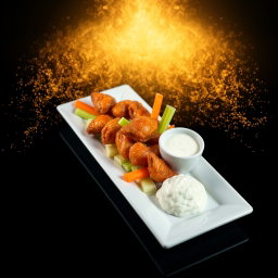 A delectable presentation of Chicken Wings served with fresh carrots, celery, and blue cheese dressing, artistically arranged on a long, narrow white rectangular plate